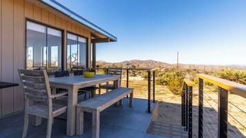 An outdoor patio with a wooden table and chairs, a bench, and a view of the desert landscape.