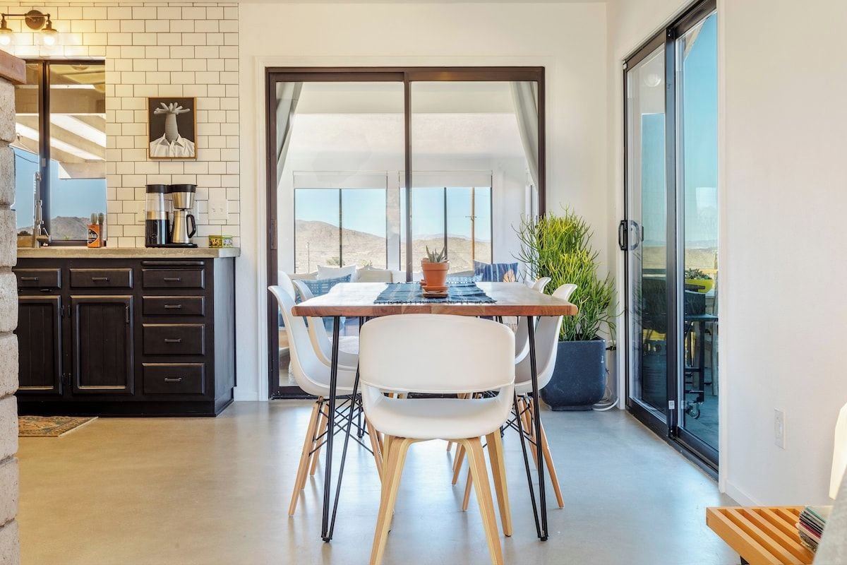A modern kitchen with a dining area, a large sliding glass door leading to a balcony, and a view of the desert.