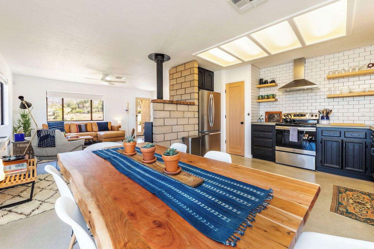 Une cuisine moderne avec une cheminée en briques, des appareils électroménagers en acier inoxydable et un coin repas comprenant une table et des chaises en bois.