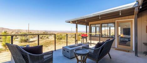 A balcony with wicker furniture, a fire pit, and a view of the desert.