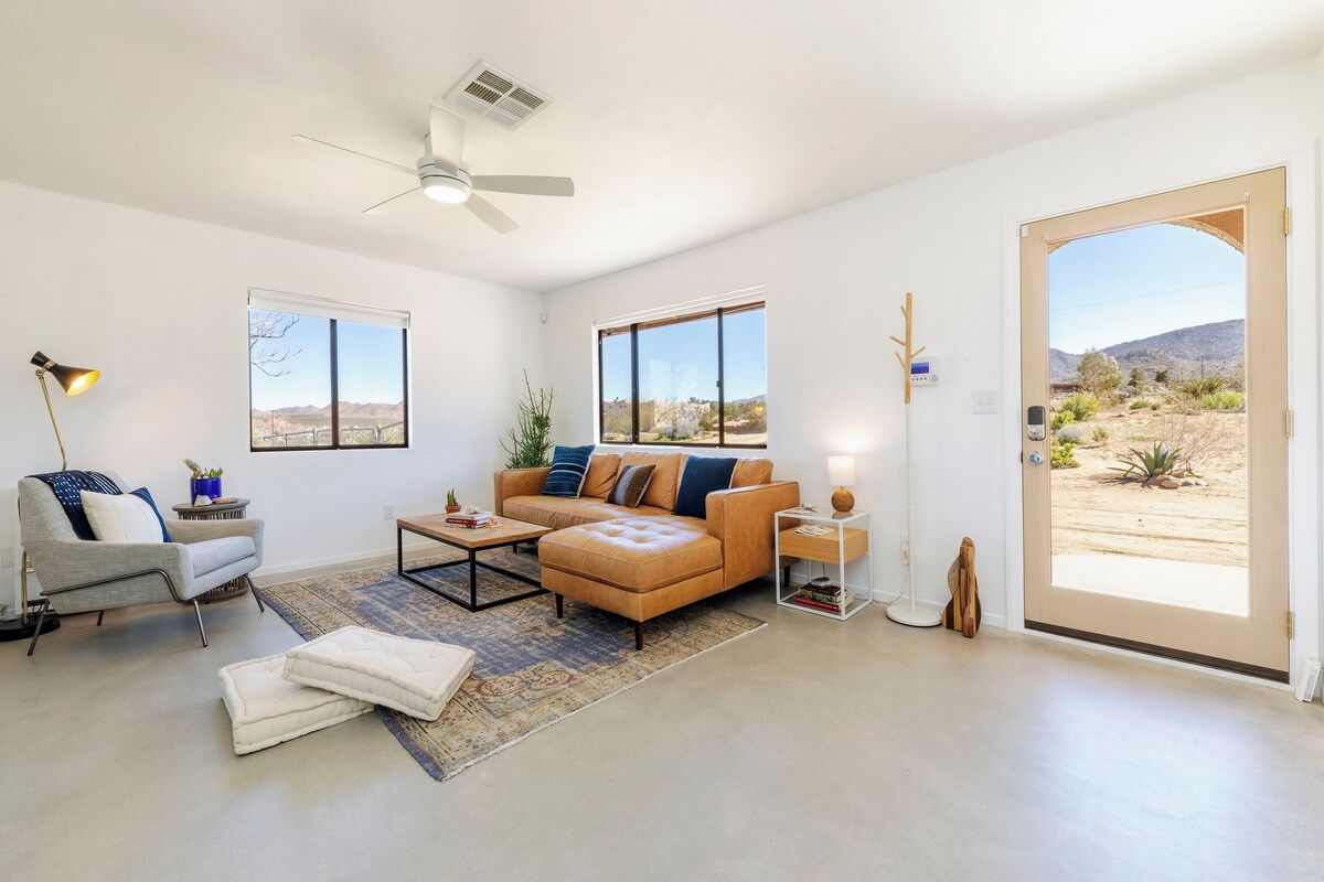 A modern living room with a sofa, coffee table, and a large window offering a view of a desert landscape.