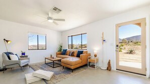 A modern living room with a sofa, coffee table, and a large window offering a view of a desert landscape.