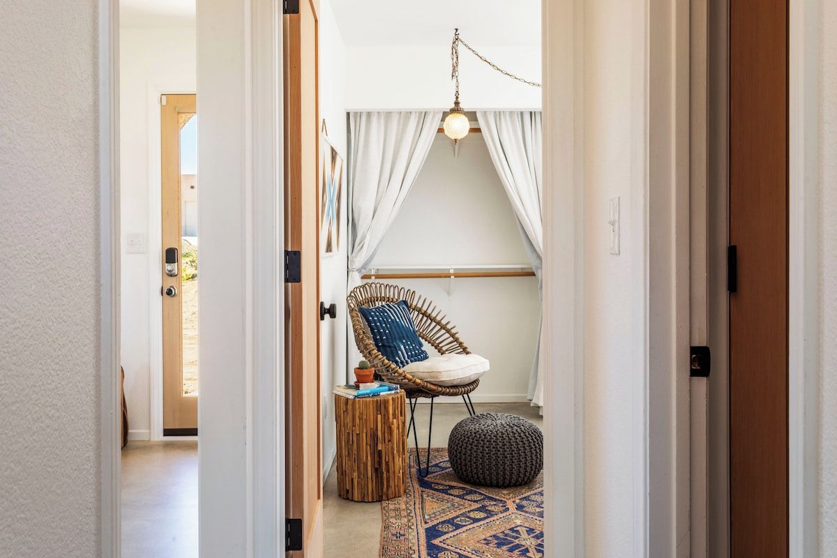 A hallway leading to a room with a wicker chair, a small round table, and a hanging light fixture.