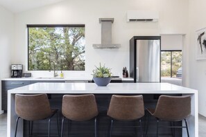 A modern kitchen with a large island, bar stools, a window with a view of trees, and a stainless steel range hood.