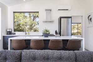 A modern kitchen with a large island, bar stools, a view of trees, and a built-in stove.