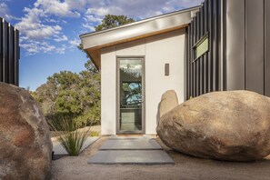 A modern building with a minimalist design, featuring a large glass door and a concrete pathway leading to the entrance.