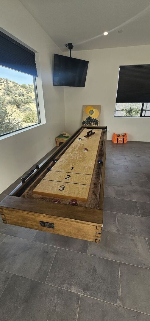 Een kamer met een jeu de boules tafel, een aan de muur bevestigde televisie en een raam met uitzicht op een woestijnlandschap.