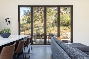 Un interior moderno con zona de comedor, sofá y un amplio ventanal corredero que da a un patio exterior.
