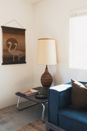Ein Wohnzimmer mit einem blauen Sofa, einer Lampe, einem gerahmten Bild und einem kleinen Tisch mit einem Buch.