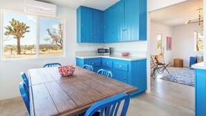 A modern kitchen with blue cabinets, a wooden dining table, and a view of the desert. - Flag Ranch - Hot Tub, Fire Pit and BBQ (Yucca Valley)