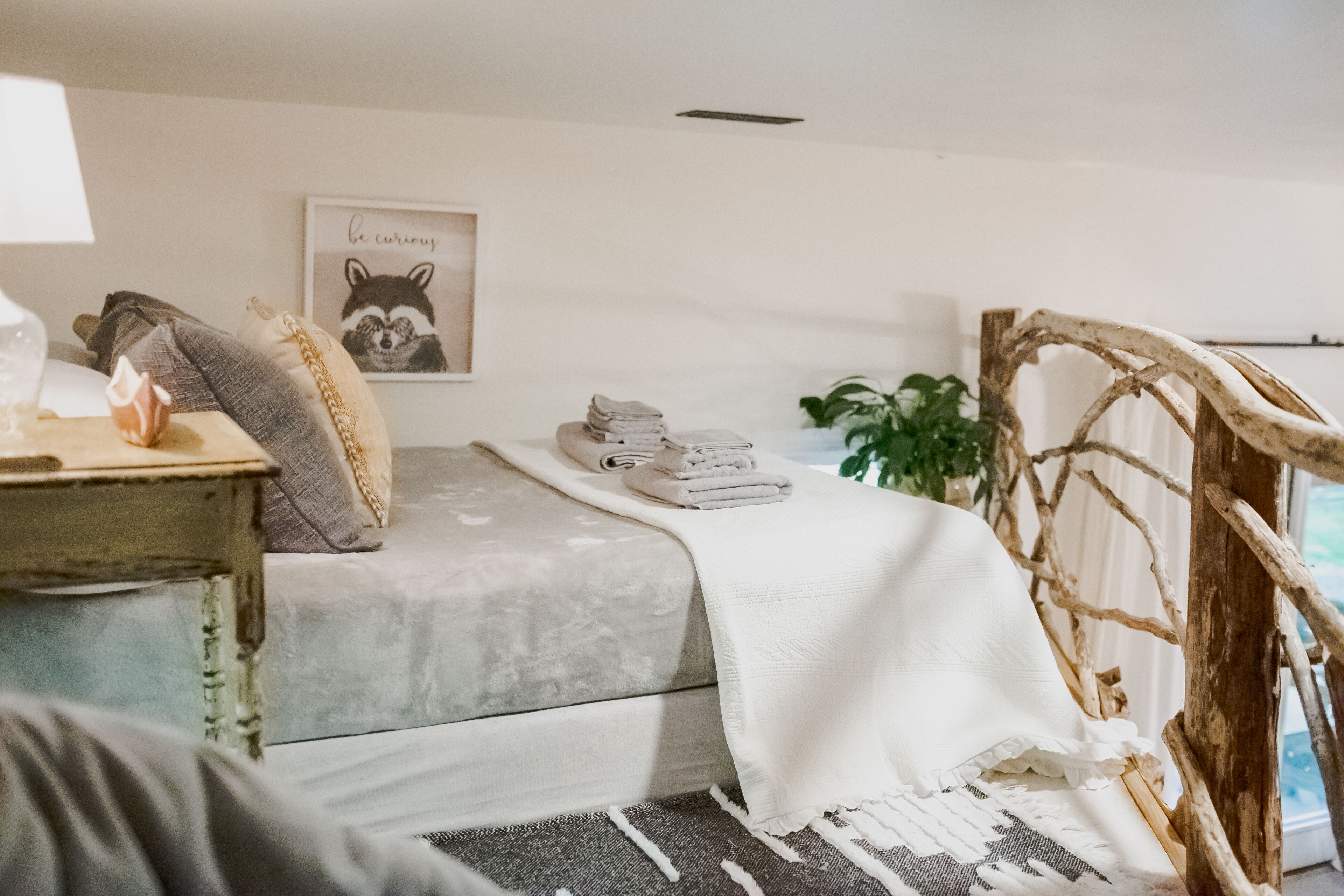A cozy room with a bed, a side table with a lamp, a framed picture on the wall, and a wooden chair.