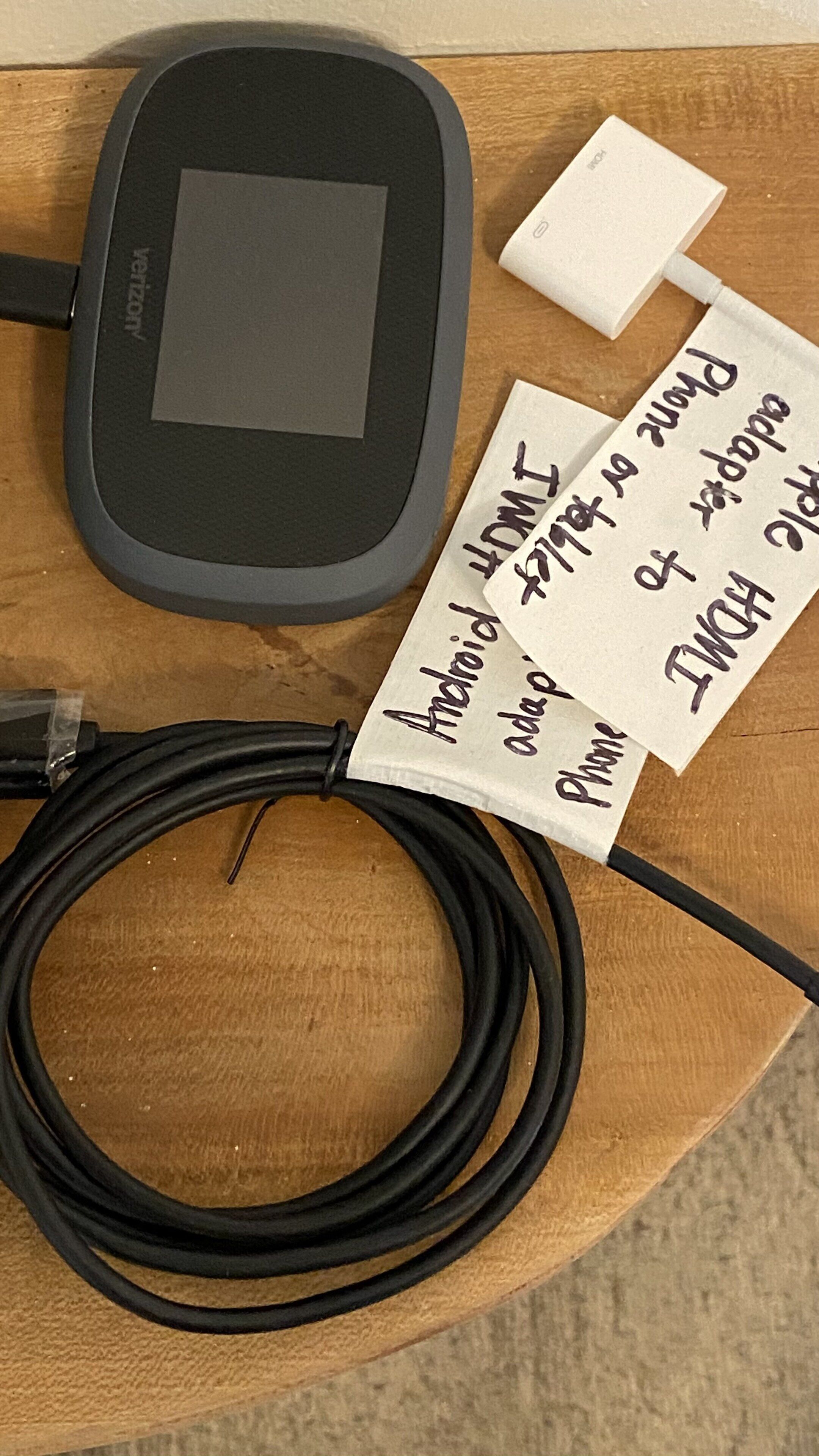 Una tableta, un cable USB y una nota escrita a mano sobre una superficie de madera.
