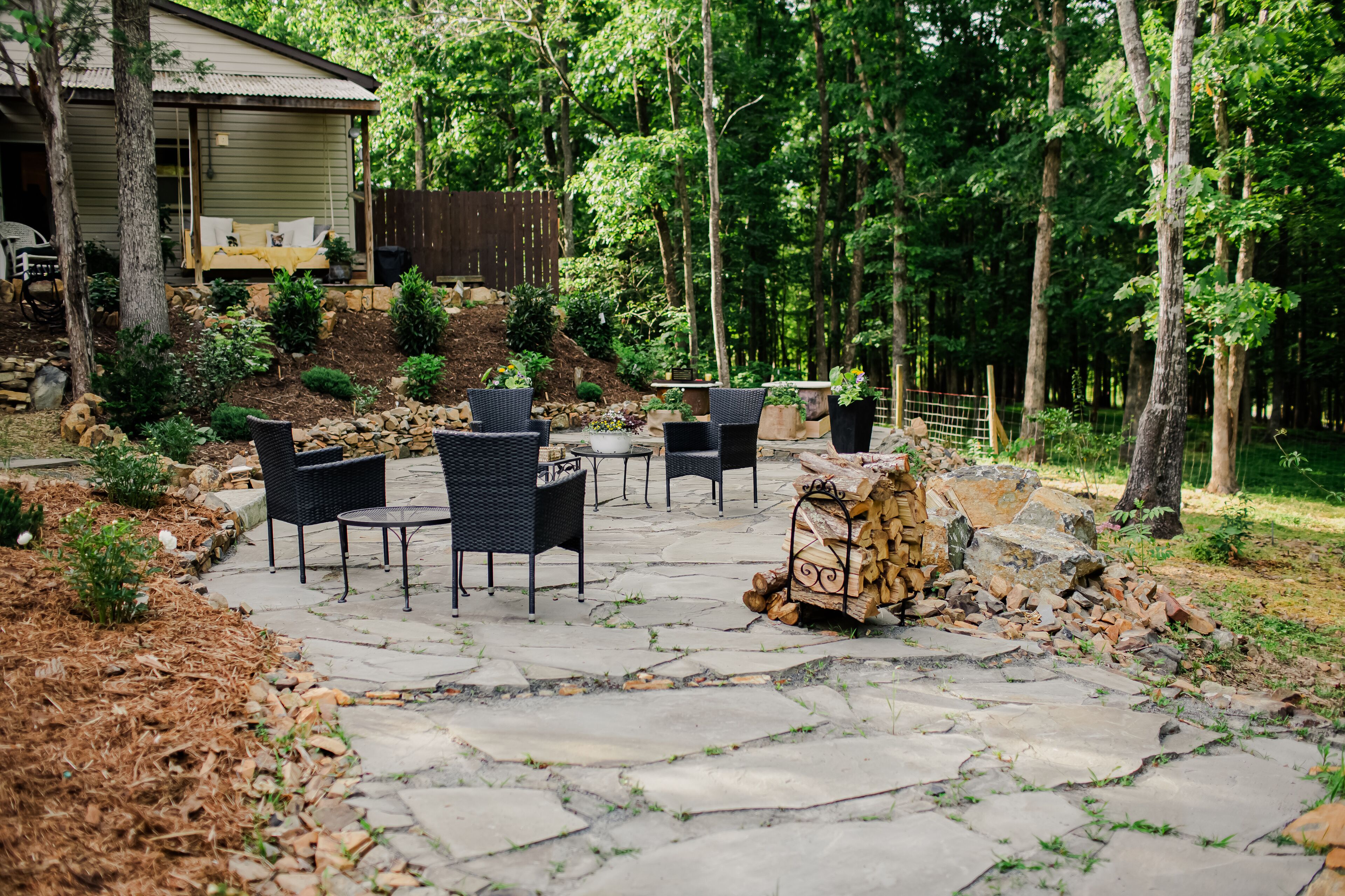 A stone patio with outdoor furniture, a fire pit, and a stack of firewood.