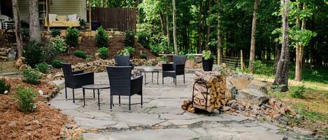 A stone patio with outdoor furniture, a fire pit, and a stack of firewood.