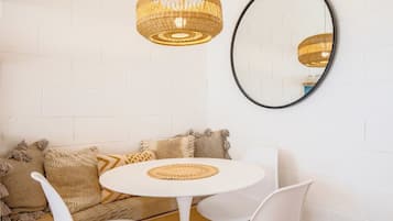 A room with a white brick wall, a round table with chairs, a woven pendant light, and a round mirror.