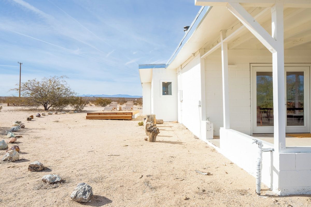 A modern building with a covered patio area, a clear view of the surrounding desert landscape, and a series of rocks arranged in a line.