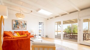 A spacious living room with a bright ceiling, a large window, and a view of the outdoors. - That Desert House - Hot Tub, Privacy & Desert Views! (Twentynine Palms)