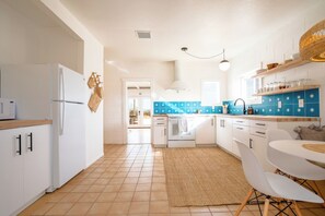 Une cuisine moderne avec des meubles blancs, un réfrigérateur blanc, un pare-feu en carreaux bleus et un coin repas comprenant une table ronde et des chaises blanches.
