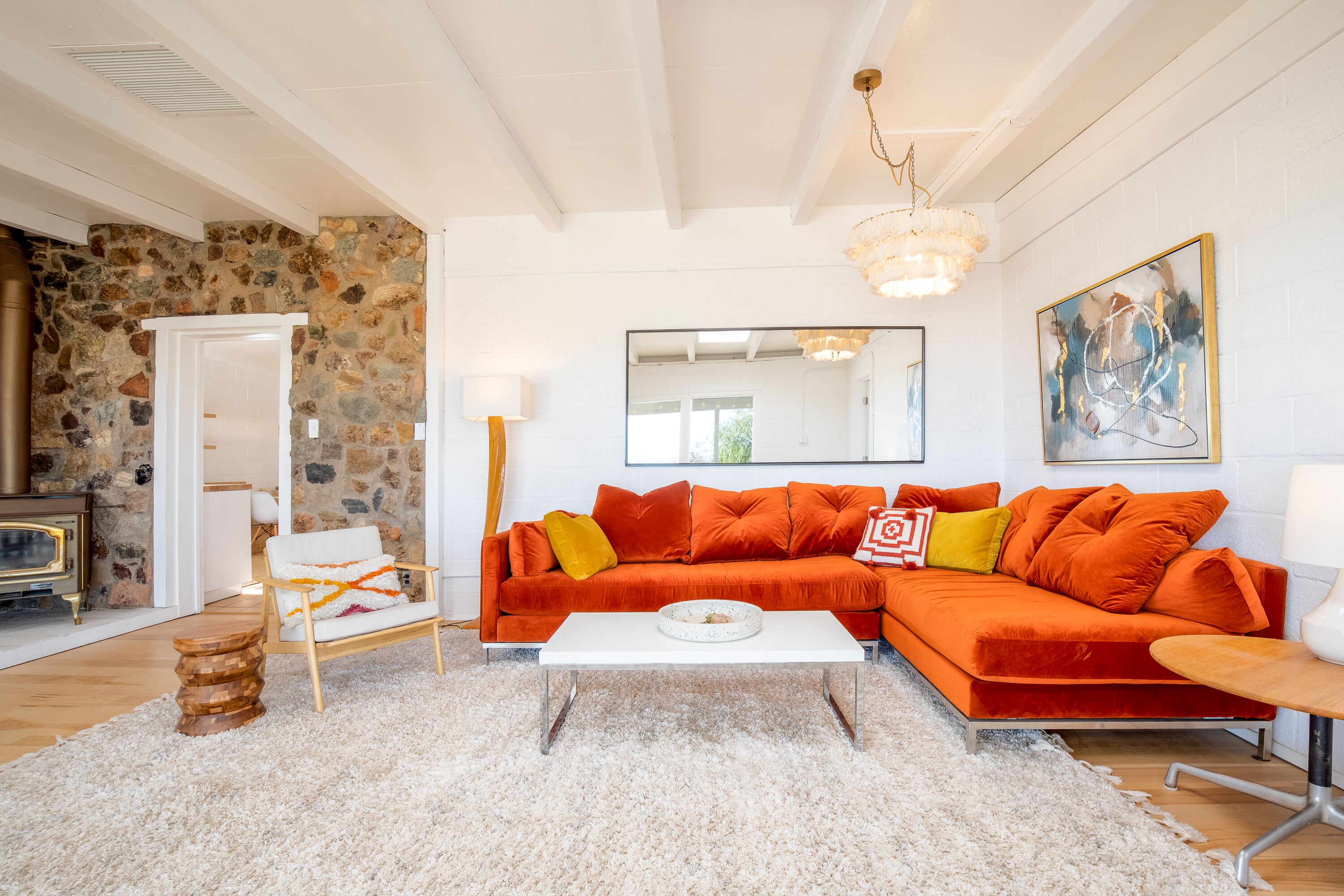 Ein Wohnzimmer mit einer Steinwand, einem weißen Sofa mit orangen Kissen, einem weißen Couchtisch und einem Holznachttisch.