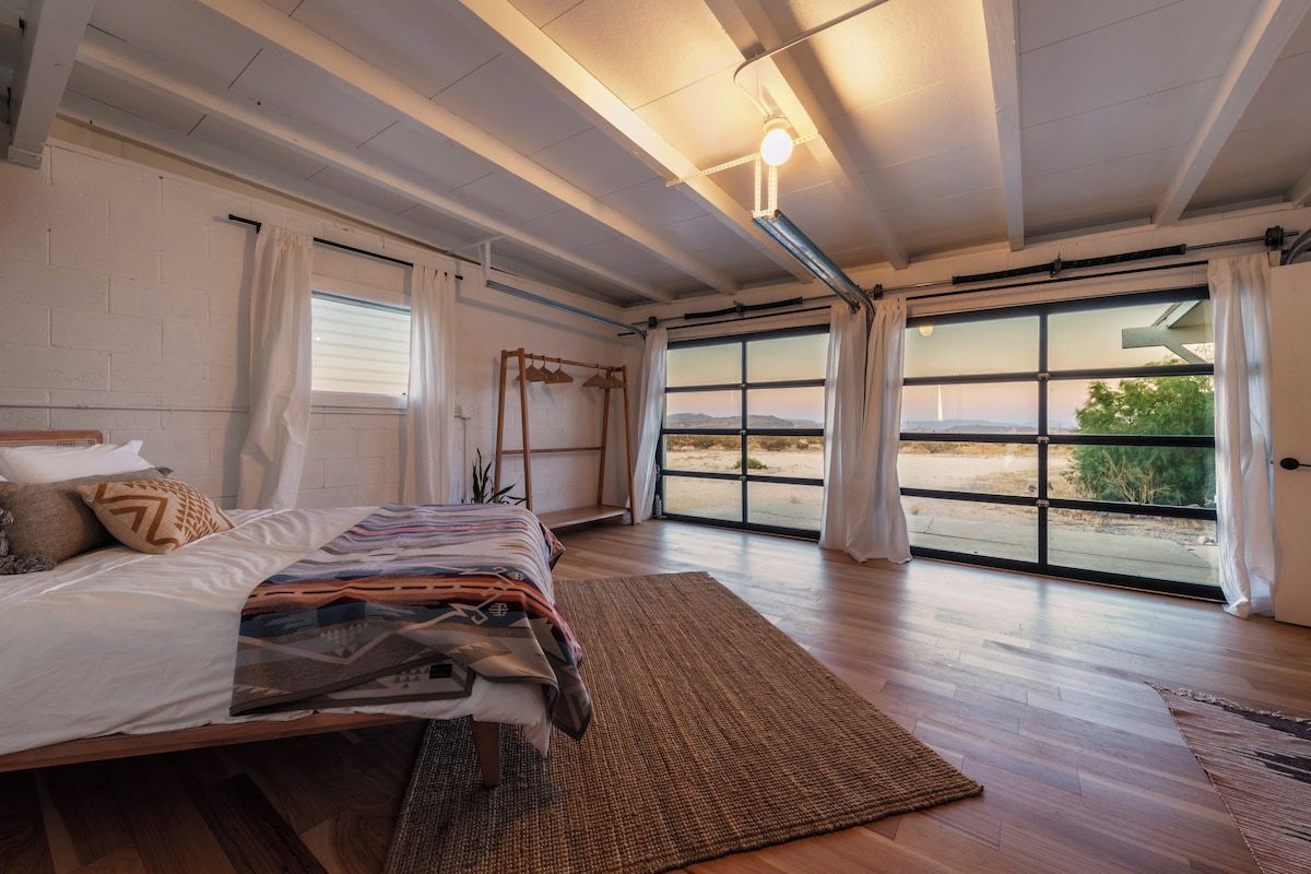 Un dormitorio con una cama grande, una ventana con cortinas y vistas al exterior.