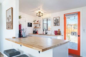 A modern kitchen with a wooden countertop, a built-in sink, and a red-framed door leading to an outdoor area. - Walpi Ranch - Joshua Tree Getaway with Hot Tub! (Joshua Tree)