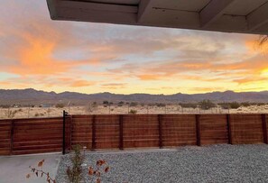 A view of a desert landscape with mountains in the distance, a wooden fence, and a gravel area in the foreground.