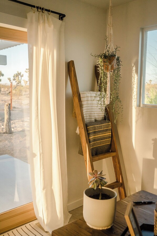Une pièce avec une chaise en bois, une plante suspendue, une fenêtre donnant sur un paysage désertique et un rideau.