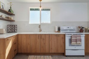 Une cuisine avec des meubles en bois, un plan de travail blanc, un four encastré et une fenêtre au-dessus de l’évier.