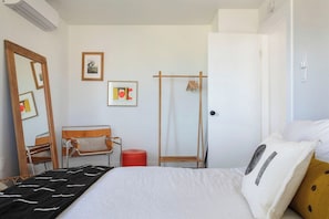 Une chambre à coucher avec un lit, une chaise en bois, un tabouret rouge, une armoire en bois et un miroir.