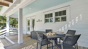 Eine überdachte Terrasse im Freien mit Holzdeck, einem Tisch mit Stühlen und einem Fenster mit Rollläden.