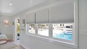 Ein Zimmer mit großem Fenster und Blick auf einen Swimmingpool, einem Bett mit gestreifter Bettdecke und einer Tür, die nach draußen führt.
