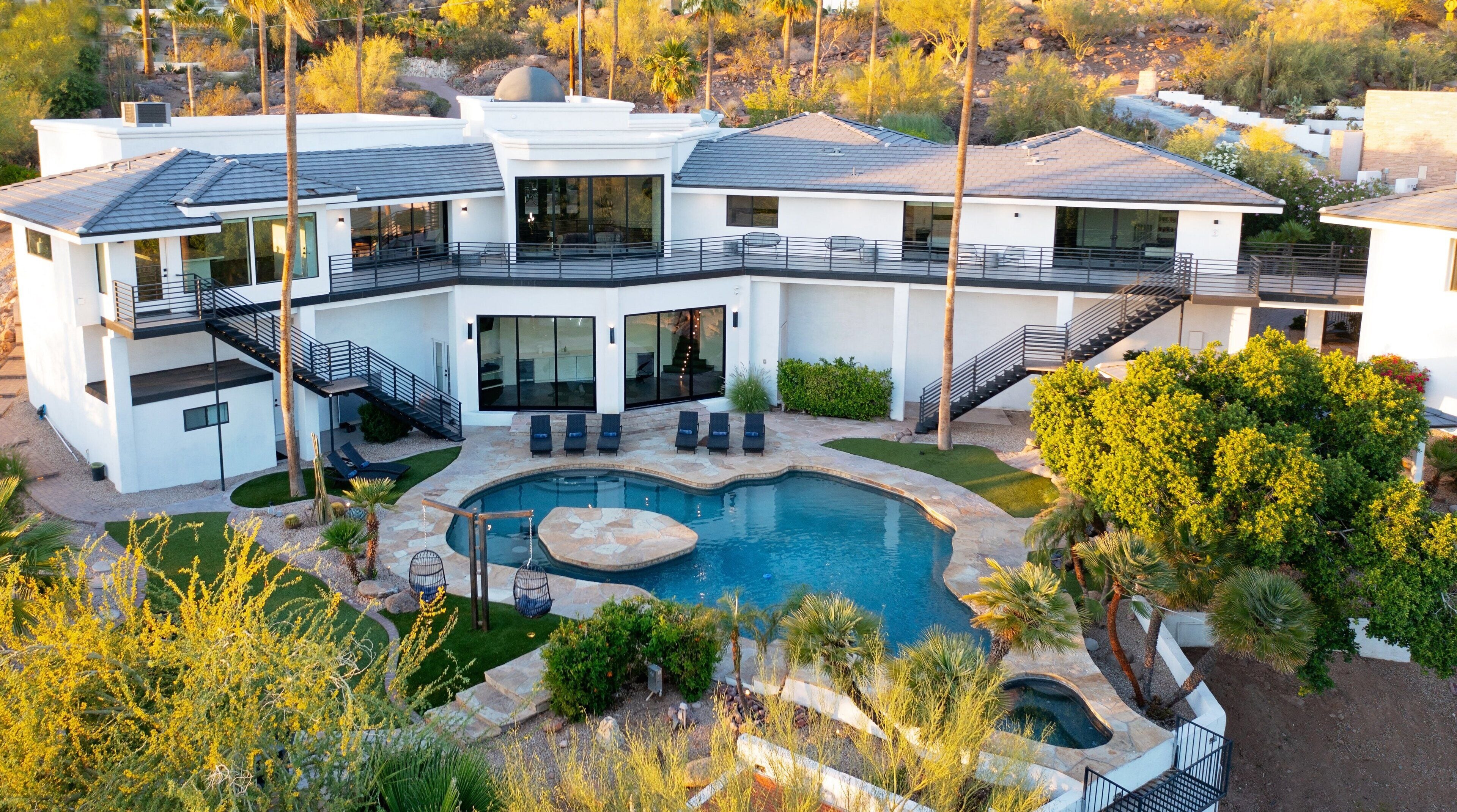 A modern multi-story house with a swimming pool, outdoor seating, and a landscaped garden.