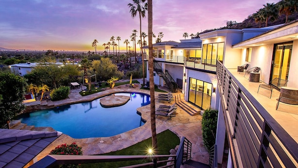 Une maison moderne dotée d’une piscine, d’un espace extérieur aménagé et offrant une vue sur la ville au crépuscule.
