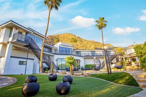 A modern multi-story house with a landscaped garden, outdoor seating, and a mountain backdrop. - Camelback Mountain Mansion - Micro-resort, Views, Golf, Heated Pool, Game Room (Phoenix)