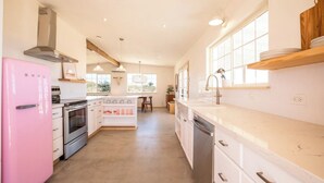 A modern kitchen with a pink refrigerator, stainless steel appliances, and a central island with a sink and stools. - Flamingo Ranch - Dreamy Desert Design (Yucca Valley)
