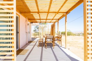 Een overdekt buitengebied met een houten pergola, een tafel en stoelen, en uitzicht op het woestijnlandschap.