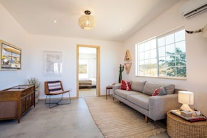 A spacious living room with a sofa, a coffee table, a chair, and a large window offering a view of the outdoors.