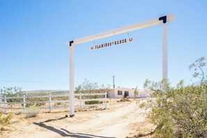 A wooden gate with a sign reading 'FLAMINGO RANCH' in a desert landscape with sparse vegetation and a clear sky.