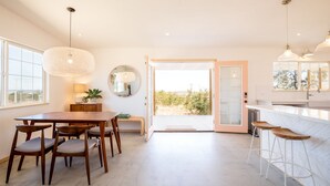 Eine moderne Küche mit Essbereich, ausgestattet mit einem großen Tisch, Barhocker, Pendelleuchten und Blick durch die offene Tür.