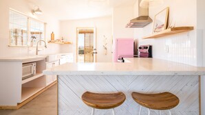 Eine moderne Küche mit einer weißen Marmorinsel, Holzbarhocker, Pendelleuchten und einem pinken Kühlschrank.