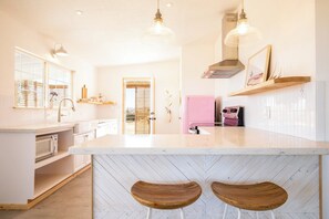 A modern kitchen with a central island, two wooden stools, pendant lighting, and a pink refrigerator.