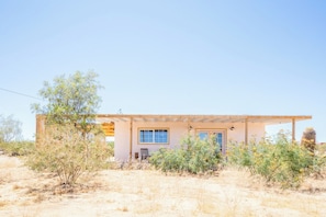 A single-story house with a flat roof, a covered porch, and a small front yard with sparse vegetation.