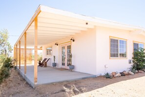 Een gelijkvloers huis met een overdekte veranda, een voordeur en een klein terras met tuinmeubilair.