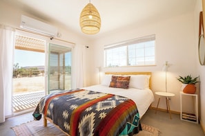 A bedroom with a bed, a window, a ceiling fan, and a door leading to an outdoor area.