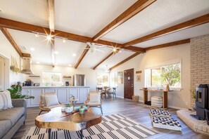 A spacious living area with a wooden coffee table, seating, a fireplace, and a kitchen in the background.