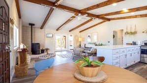 A spacious living area with a wooden ceiling, a dining table with a potted plant, and a kitchen with white cabinets.