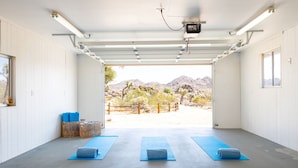 A spacious indoor area with a concrete floor, two blue yoga mats, and a view of a desert landscape through an open door.