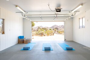A spacious indoor area with a concrete floor, two blue yoga mats, and a view of a desert landscape through an open door.