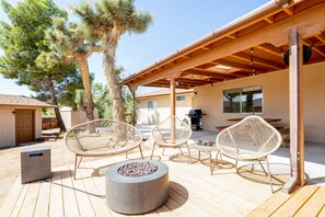 Eine Außenpatio mit Feuerstelle, Korbstühlen und einem überdachten Bereich mit einer Pergola.