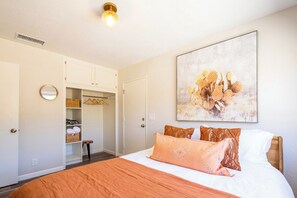 A bedroom with a bed, a wardrobe, a mirror, and a wall-mounted artwork.
